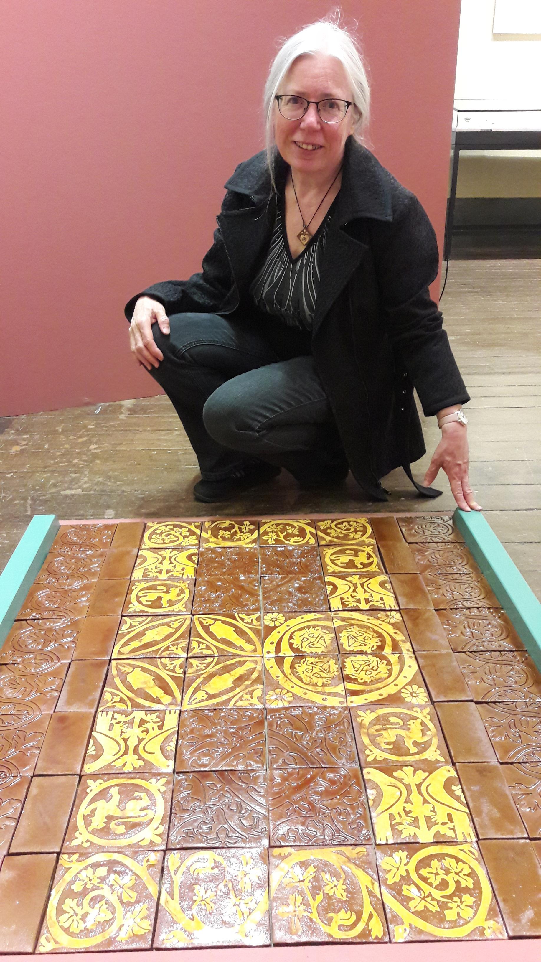 Karen Slade ak Kate Tiler witha replica medieval tile floor section made for Chester Museum in 2022..